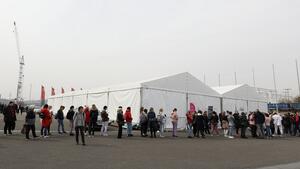 Kilkadziesiąt osób stoi w kolejce wzdłuż białego namiotu