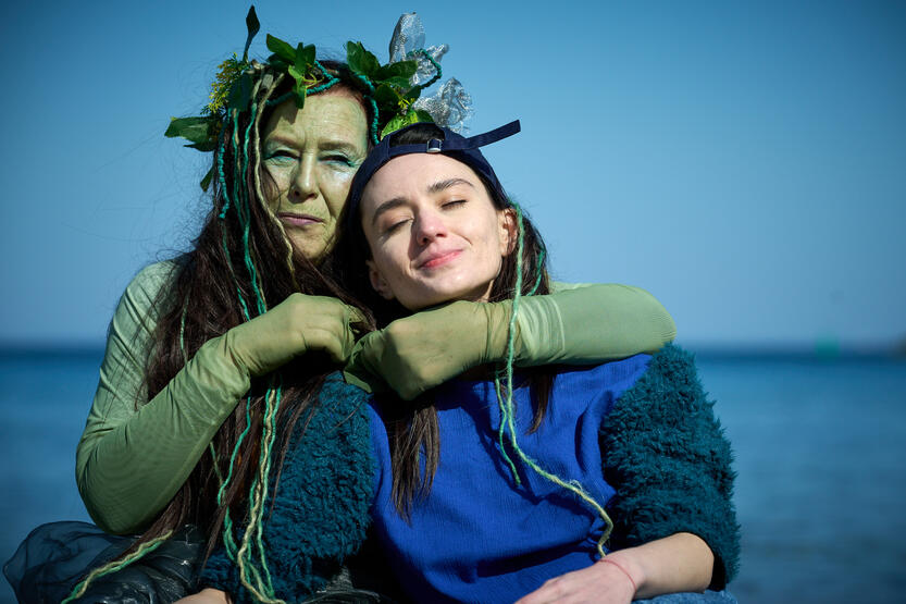 dwie aktorki przytulone do siebie na tle morza, jedna w stroju syreny