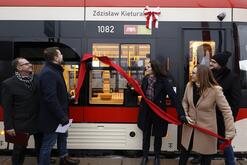 na zdjęciu prezydent gdańska, obok niej przewodnicząca miejskich radnych oraz trzech mężczyzn, ściągają uroczyście czerwoną szarfę zamocowaną na biało czerwonym tramwaju