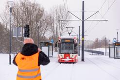na zdjęciu mężczyzna w pomarańczowej kamizelce, odwrócony plecami do fotografującego, przed mężczyzną widać biało-czerwony tramwaj, wokół mnóstwo śniegu