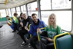 na zdjęciu grupa sześciu młodych osób, siedzą na krzesełkach w tramwaju, jeden za drugim, pozują do zdjęcia, trzymając w rękach małe ulotki