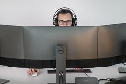 Mężczyzna w okularach ze słuchawkami na uszach siedzący przed wielkim monitorem komputera