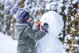 Chłopiec w czapce po lewej, po prawej bałwan z nosem z marchewki, wokoło dużo śniegu