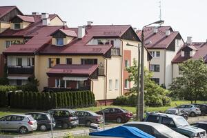 Na zdjęciu widać kilka domów jednorodzinnych w dzielnicy Matarnia, ich ściany są w kolorze bladopomarańczowym, a dachy są czerwone. Obok budynków widać kilkanaście zaparkowanych samochodów osobowych. Jest też kilka latarni ulicznych i zielone krzaki