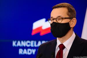 Mężczyzna w średnim wieku w okularach, gładko uczesanych (premier Morawiecki) w czarnej maseczce zasłaniającej usta i nos, w granatowym garniturze podczas konferencji prasowej