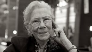 Czarno-białe zdjęcie: twarz uśmiechniętej starszej kobiety w okularach, lewa dłoń oparta o głowę
