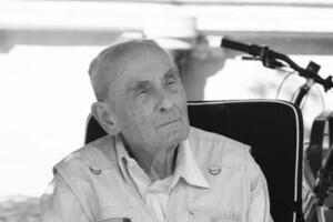 Czarno-białe zdjęcie: starszy mężczyzna siedzi w koszuli, patrzy w dal 