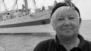 Czarno-białe zdjęcie: Uśmiechnięta kobieta w średnim wieku. W tle morze i statek