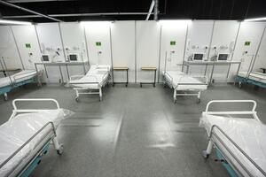 na zdjęciu sala szpitalna szpitala tymczasowego widać cztery łózka szpitalne, nowe, materace jeszcze owinięte są folią, są też monitory przy łóżkach