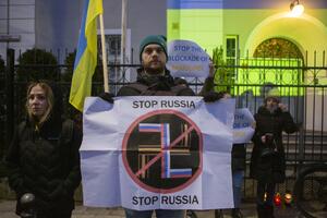 kilka osób protestujących trzyma transparenty, na pierwszym planie kolory flagi Rosji wpisane w hitlerowską swastykę, wpisaną w znak zakazu i napis Stop Russia, w tle napis Stop blokadzie Mariupola