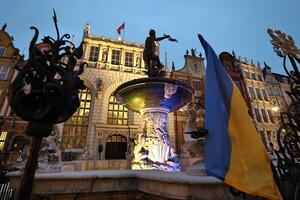 na zdjęciu fontanna neptuna, podświetlona na żółto i niebiesko, na pierwszym planie flaga ukrainy