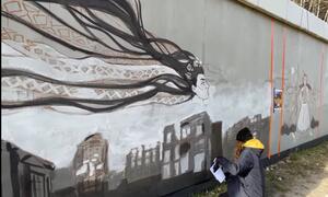 mural: nad wypalonymi budynkami widnieje kobieca twarz 