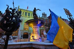 fontanna Neptuna wieczorem, niebiesko - żółta flaga obok, dwór Artusa oświetlony na zielono