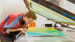 mężczyzna pochyla się nad maszyną od drukowania, ogląda kolorowe wydruki