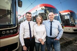 Andrii i Oksana Horaichuk oraz Dymitr Grzebieniowski pozują w koszulach pracowników GAiT na tle trzech tramwajów
