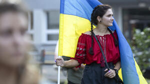Młoda kobieta w czerwonej koszuli, trzyma w żółto-niebieską flagę ukrainy. 