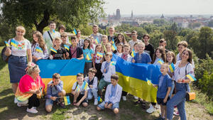 Zbiorowe zdjęcie, grupa dzieci z Ukrainy i wychowawcy na tle panoramy Gdańska widocznej z Góry Gradowej, trzymają rękach flagi Ukrainy