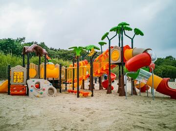 kolorowy plac zabaw ustawiony na piasku plaży, zjeżdżalnie i inne urządzenia dla dzieci, zwieńczony w formie drzew - palm