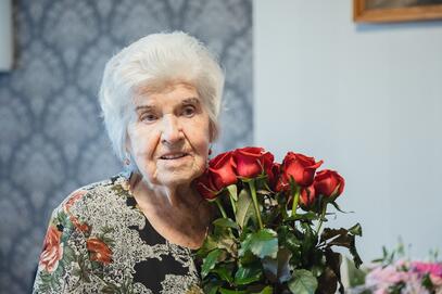 starsza osoba pozuje do zdjęcia z bukietem kwiatów