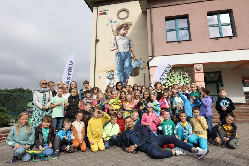 dzieci, nauczyciele i artyści pozują przed budynkiem szkoły, na której ścianie powstał mural 