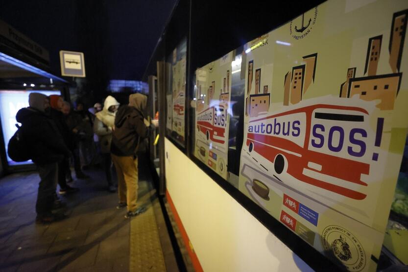 bok autobusu oklejony plakatami z napisem autobus SOS, przy otwartych drzwiach ustawiają się potrzebujący