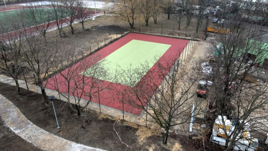 na zdjęciu z drona widać powstający kort tenisowy, jest już nawierzchnia w kolorze bordowym i wewnątrz w jasnym kolorze, obiekt otoczony jest drzewami