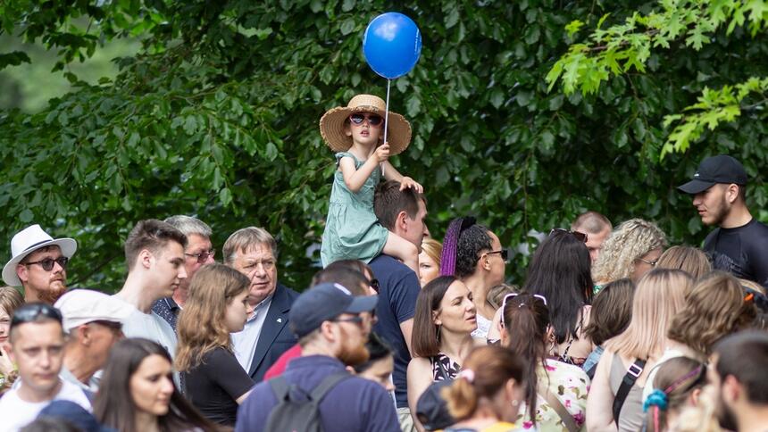 Tłum ludzi na powietrzu. U góry zdjęcia dziewczynka siedząca na ramionach mężczyzny, w dłoni trzyma na sznurku niebieski balonik 