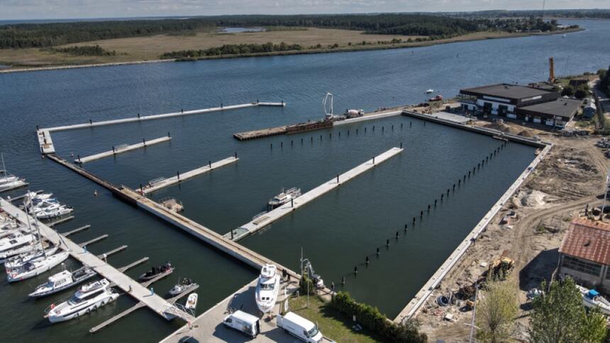 zdjęcie z drona, widać rozbudowywany port jachtowy, w tym pływające pomosty i nowy falochron, widać też sprzęt budowlany