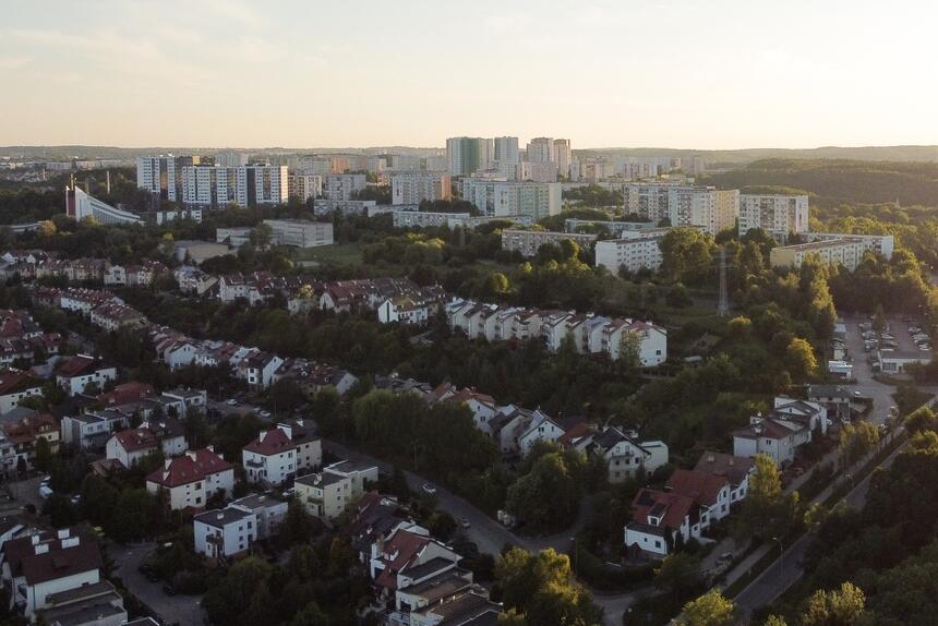 zdjęcie z drona, widać część dzielnicy piecki migowo, na pierwszym planie duża ilość domów jednorodzinnych, stojących na wzgórzu, w tle widać kilka wieżowców mieszkaniowych, zdjęcie wykonane o wschodzie słońca