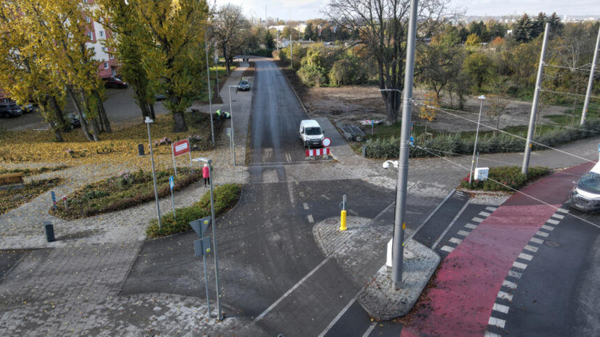 na zdjęciu z drona widać skrzyżowanie dwóch ulic, widać jezdnie i chodniki, rosnące wokół jesienne drzewa, na skrzyżowaniu stoi samochód, po lewej na chodniku widać pieszego