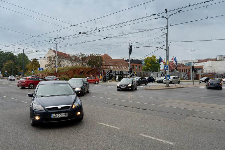 Skrzyżowanie ulic z torowiskiem tramwajowym, na nim samochody, nad nimi tramwajowa trakcja elektryczna 