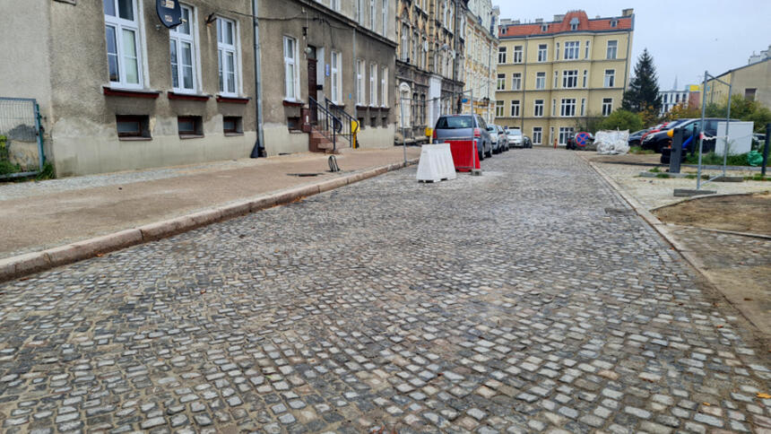na zdjęciu widać fragment brukowanej ulicy, po lewej fragment chodnika a za nim widać fragment kamienicy