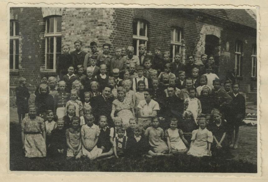 czarno-białe archiwalne zdjęcie zbiorowe grupy dzieci i kilku dorosłych na tle ceglanego budynku