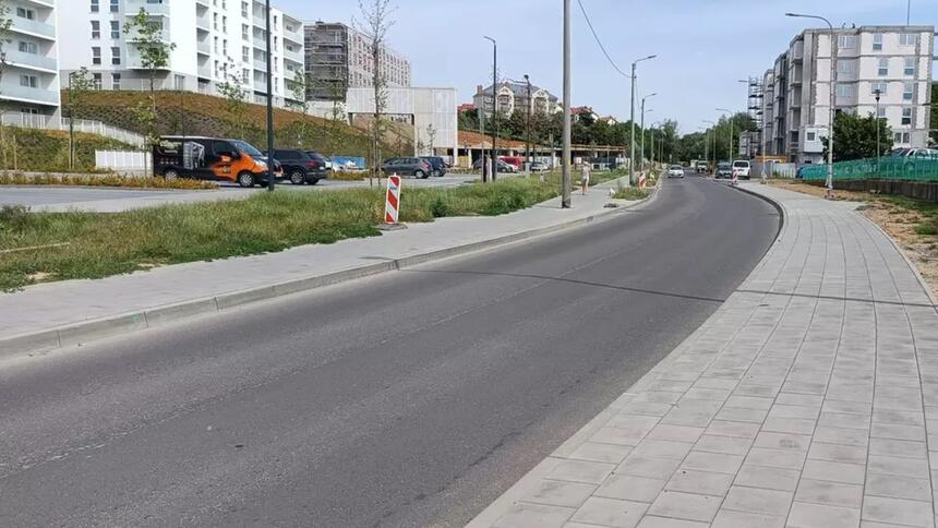 Widok ulicy, na której ułożono nowy asfalt. Wokół znajdują się nowe bloki mieszkalne