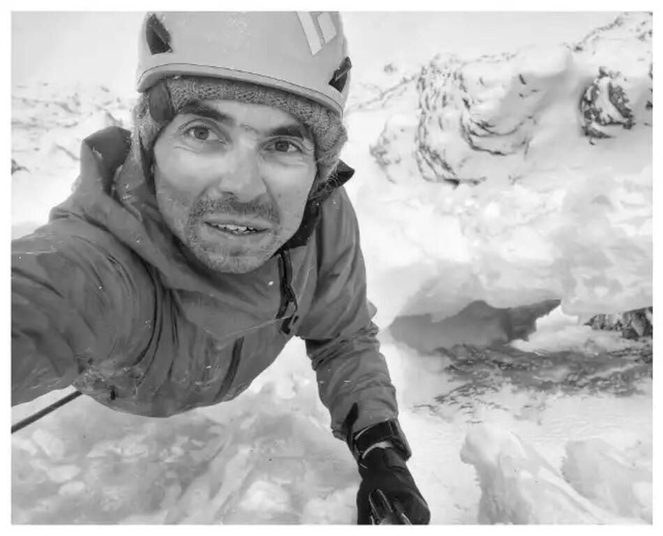 Twarz mężczyzny w kasku, w tle stok zimą (czarni-białe zdjęcie typu selfie)