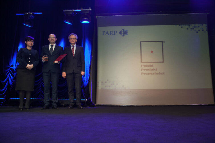 Prezes AssisTech Bartosz Kunka (stoi w środku) odebrał nagrodę z rąk prezes PARP Bożeny Lublińskiej-Kasprzak, przewodniczącej kapituły konkursu. Na zdjęciu także prof. Wojciech Dominik, członek kapituły.
