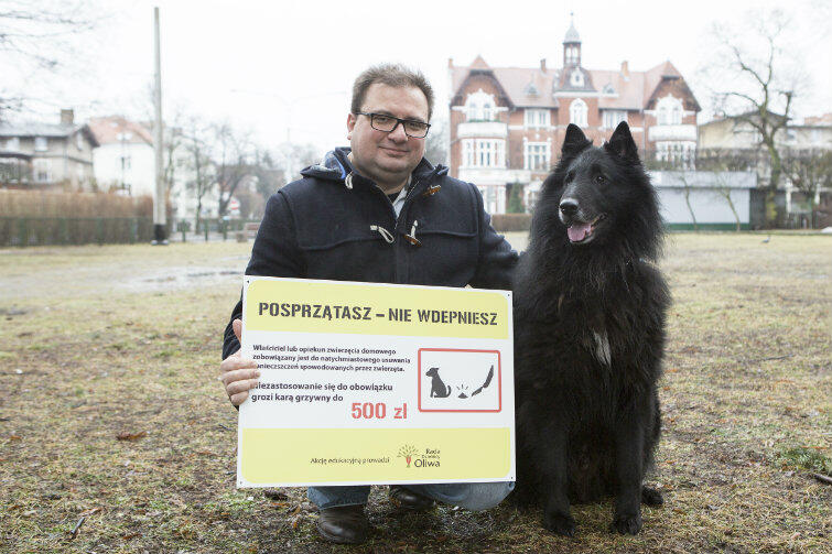 Radny dzielnicowy Tomasz Strug prezentuje tablicę, która ma przypominać właścicielom psów, że kupy po swoich pupilach powinni sprzątać.

