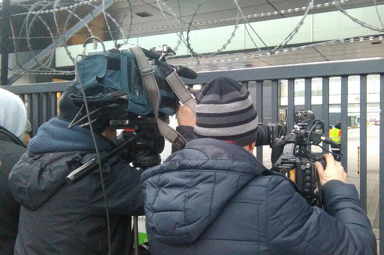 Kamery stacji newsowych za płotem lotniska próbują wypatrzyć Lecha Wałęsę w drodze z samolotu do terminalu. 
