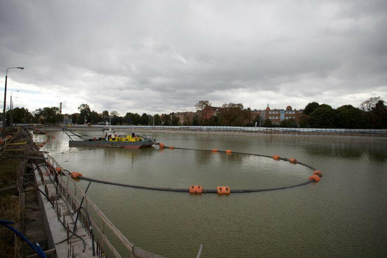 Wrzesień 2013 r. Prace budowlane trwają. Na basenie wypełnionym wodą pływa barka podająca cement.
