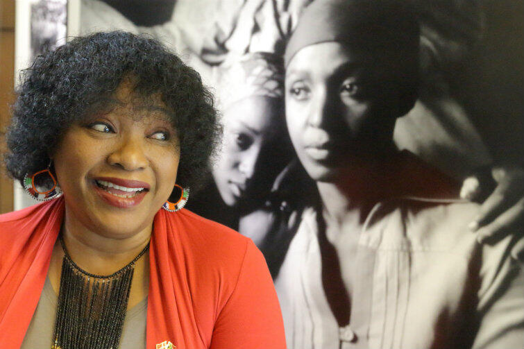 Zindzi Mandela pozuje na tle zdjęcia przedstawiającego ją w latach młodości.
