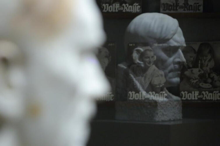 Rzeźba odbija się w szybach gabloty, w której leżą numery rasistowskiego i antysemickiego pisemka Volk und Rasse
