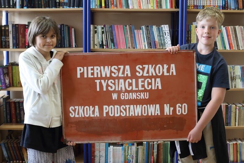 Maria i Damian, uczniowie Szkoły Podstawowej nr 60 trzymają tablicę wiszącą pierwotnie na budynku szkoły 