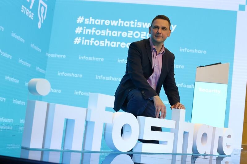 Grzegorz Borowski prezes zarządu Infoshare w studiu konferencji w Amber Expo, 24 września 2020, przyklęka na scenie za białymi literami układającymi się w napis infoshare. jest uśmiechnięty, ubrany w granatowy garnitur