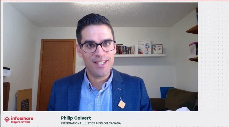  Philip Calvert z International Justice Mission Canada przemawia na scenie Inspire podczas Infoshare 2020 online, widać zrzut ekranu, na którym widać mężczyznę w okularach, młodego, w niebieskiej marynarce, ujęcie do pasa, przemawia z ekranu komputera prawdopodobnie w swoim domu, za nim widać drzwi wyjściowe z pokoju