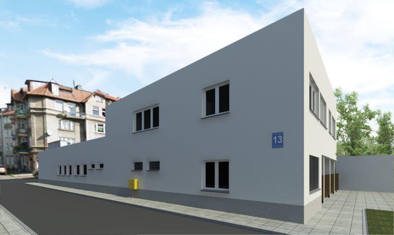 Na obrazku biały budynek (widoczne dwie ściany zewnętrzne) z kilkunastoma oknami. Na ścianie niebieska tablica z nazwą ulicy i numerem (Królikarnia 13). Przy budynku chodnik i asfaltowa droga. W tle po lewej fragment budynku mieszkalnego, po prawej drzewa. 