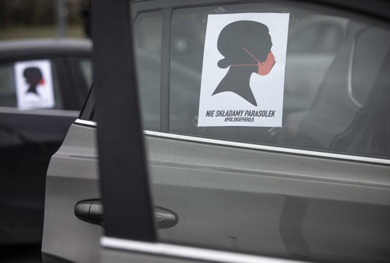 na szybie samochodu widnieje plakat - na rysunku jest czarny graficzny profil kobiety z czerwoną maseczką na ustach