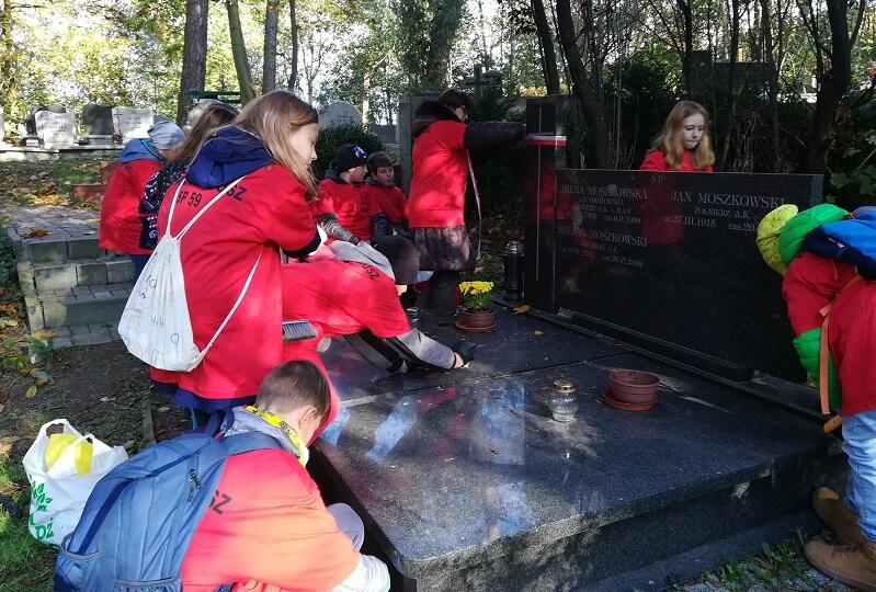 Grupa dzieci w czerwonych koszulkach sprząta grób