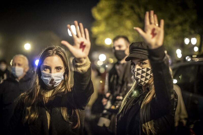 Dwie młode kobiety na Targu Drzewnym w Gdańsku. Jest wieczór, wokół trwa manifestacja. Kobiety demonstrują narysowany na wewnętrznej powierzchni dłoni znak protestu - czerwony piorun