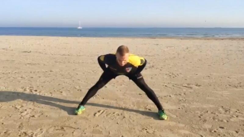 Mężczyzna ćwiczący na plaży: pochyla się do przodu na rozszerzonych nogach