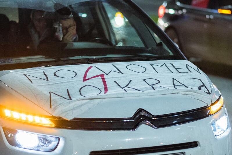 maska białego samochodu, jest na na niej rozpięty napis: "no woman no kraj" i czerwona błyskawica